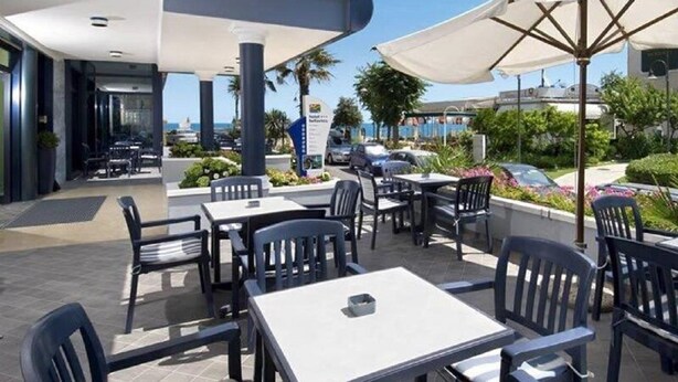An outdoor patio area with tables and chairs, umbrellas, and a view of the sea. - Hotel Bellavista (Gabicce Mare)