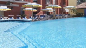 A swimming pool with clear blue water, surrounded by lounge chairs and umbrellas. - Hotel Bellavista (Gabicce Mare)