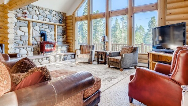 A log cabin interior with stone walls, large windows, a fireplace, leather sofas, and a television. - Breck Cabin/ Mins from Town & Lifts/ Hot Tub (Breckenridge)