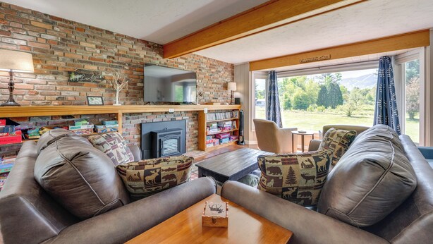 Una sala de estar acogedora con chimenea de ladrillo, sofá de cuero y un amplio ventanal con vistas al exterior.