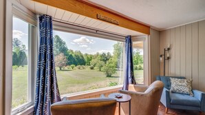 Una habitación con un ventanal grande, dos sillas, una mesita y un sillón azul.