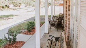 A covered porch with a bench and chairs, brick walls, and a view of the street. - 3BR/2BA w/GOLF CART!! Close to Beach & Downtown Ocean Springs! Southern Exposure (Ocean Springs)
