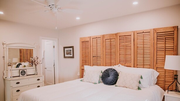 A bedroom with a bed, a dresser, a mirror, a ceiling fan, and a wooden headboard. - 3BR/2BA w/GOLF CART!! Close to Beach & Downtown Ocean Springs! Southern Exposure (Ocean Springs)