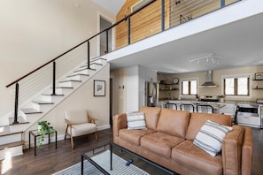Relax in this open-plan living space with a high ceiling, featuring a comfortable sofa and a well-equipped kitchen area.