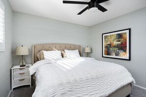 A bedroom with a bed, two bedside tables with lamps, a ceiling fan, and a framed abstract painting on the wall. - Old Town Scottsdale Family Retreat, Heated Pool, Spa, EV, Bikes, Pet-Friendly (Scottsdale)