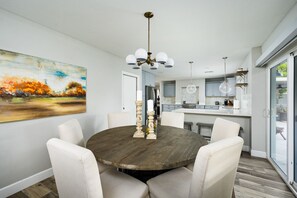 Un coin repas avec une table ronde en bois, des chaises blanches et un tableau accroché au mur.