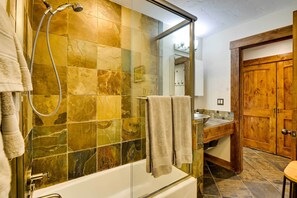 Ein Badezimmer mit Duschkabine, Badewanne, Holztür und Waschbecken mit Spiegel.