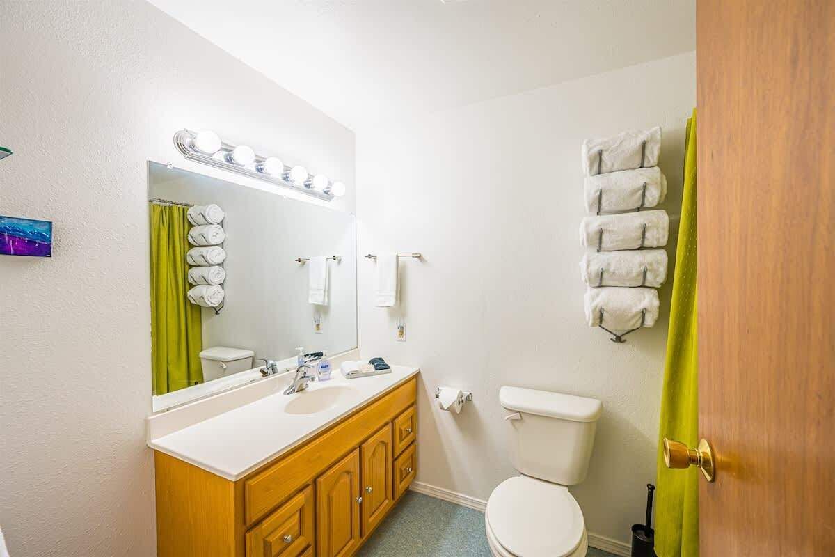 Une salle de bain avec un lavabo blanc, un meuble-lavabo en bois, un miroir avec éclairage intégré, des toilettes et un porte-serviettes.