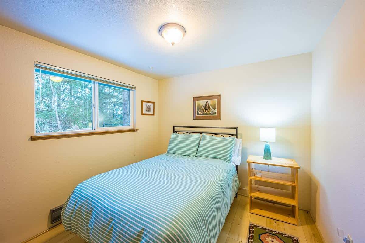 A bedroom with a bed, a window, a bedside table with a lamp, and a framed picture on the wall.