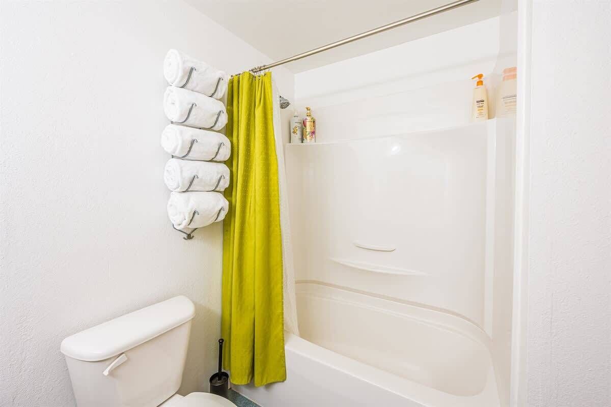 Un baño con inodoro blanco, ducha con cortina verde y artículos de aseo en la repisa.