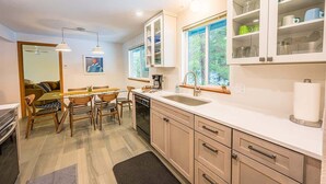 Cozinha moderna com armários de madeira, sala de jantar com mesa e cadeiras, e uma janela grande que traz luz natural.