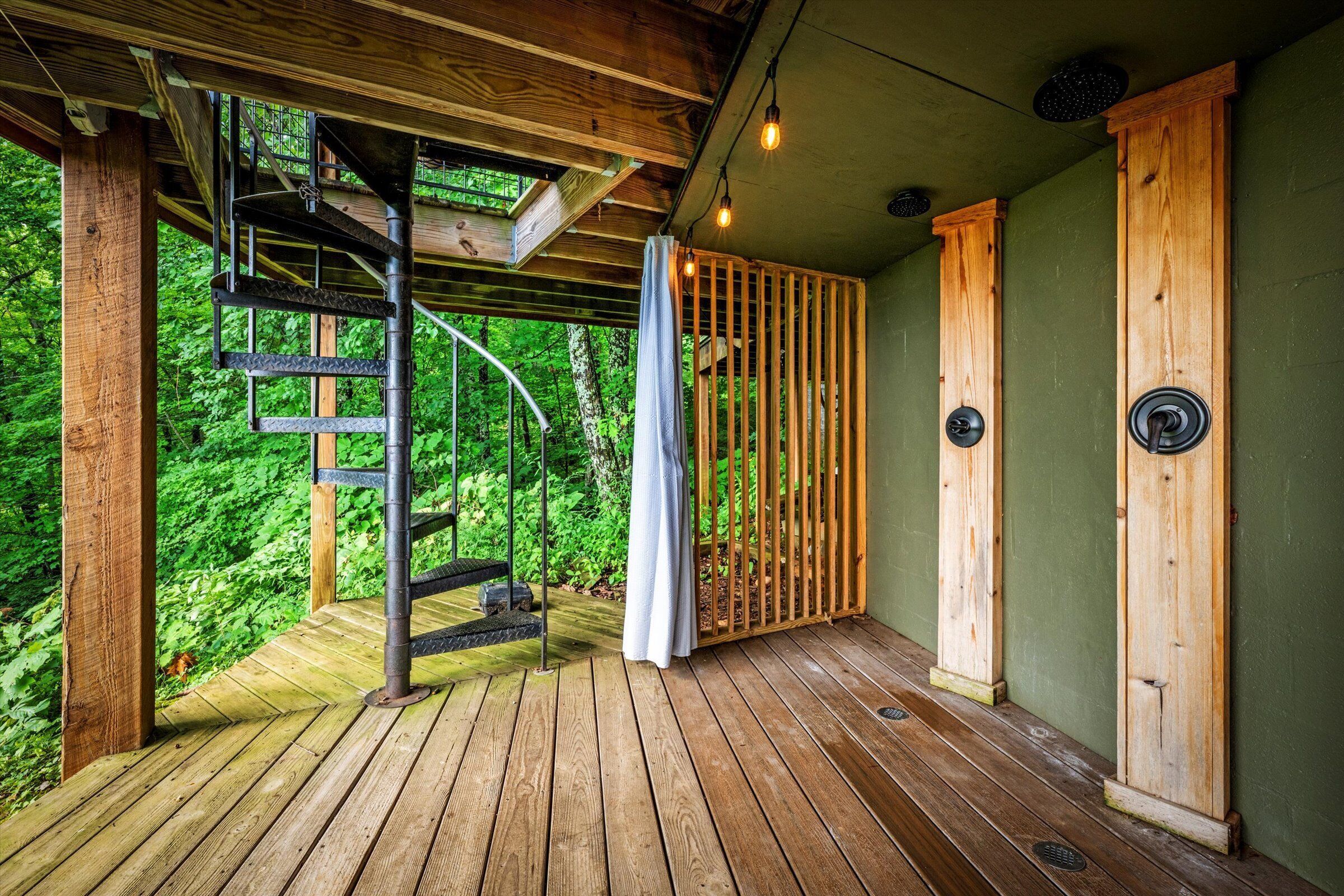 A wooden deck with a spiral staircase leading to an upper level, surrounded by lush greenery.