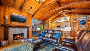 L’intérieur d’un chalet confortable, avec une cheminée, des canapés en cuir et un téléviseur fixé au mur.