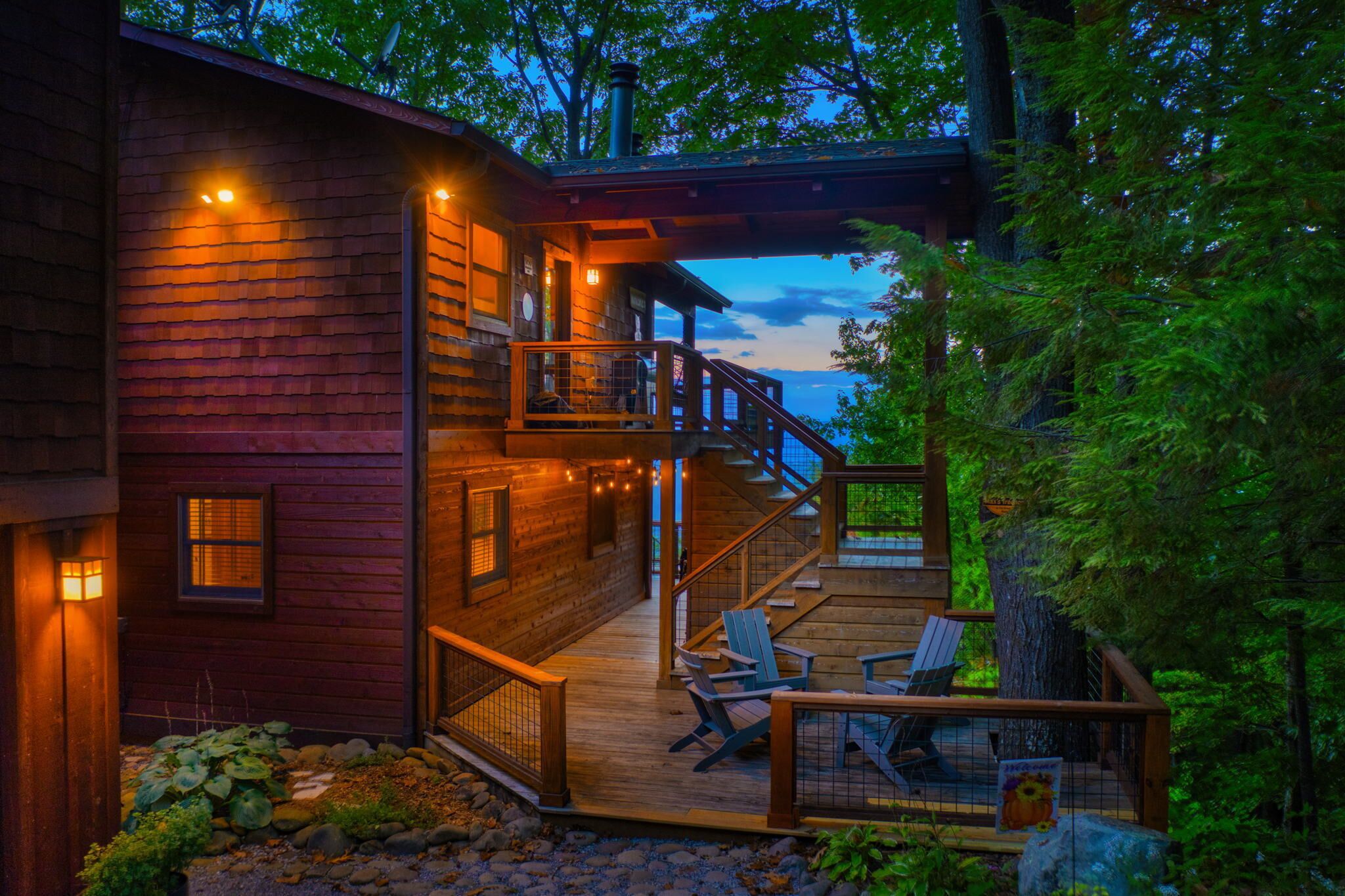 A wooden cabin with a wooden deck, outdoor seating, and a staircase leading to a balcony.