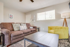 Ein Wohnzimmer mit braunem Ledersofa, einem Holztisch, einem gelben Sessel, einer Stehlampe und einem Fenster mit Jalousien.
