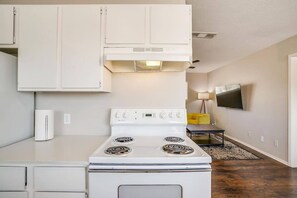 Uma cozinha compacta com armários brancos, um fogão e uma TV fixada na parede.