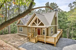 A two-story cabin with a front porch, a chimney, and a deck.