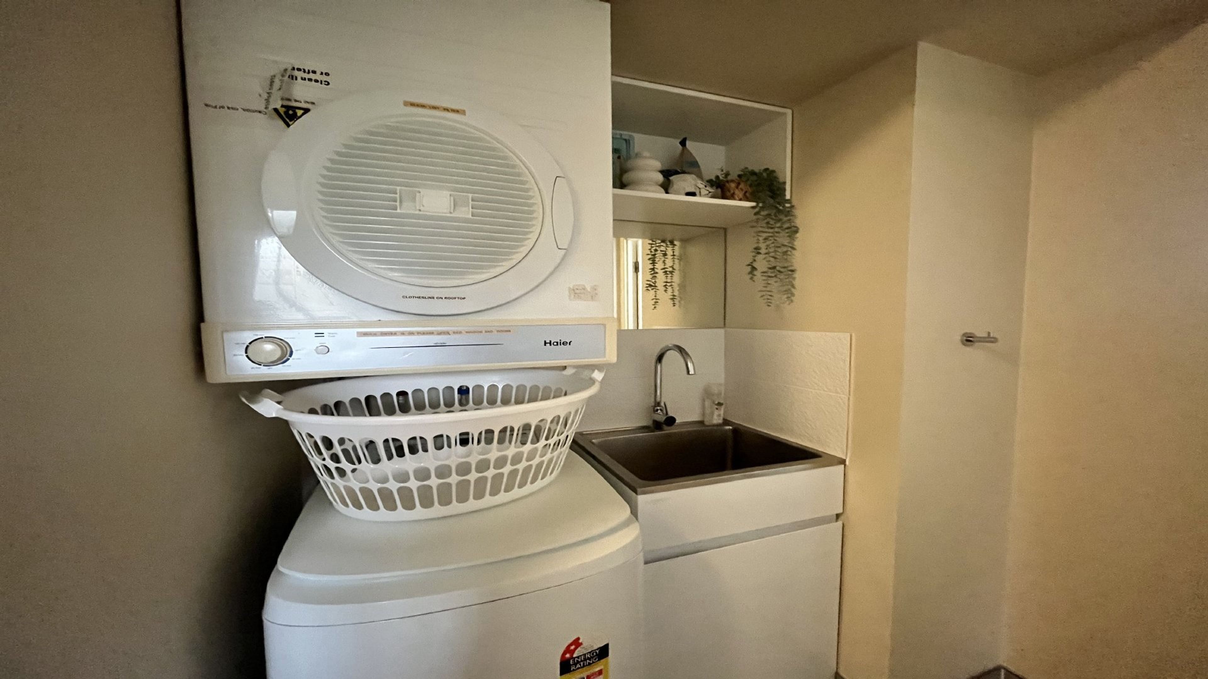 A compact laundry area with a front-loading washer and dryer, a sink, and a basket.