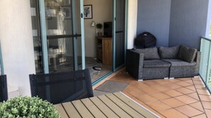 Een overdekt terras met een bank en een sofa, een glazen deuropening en een betegelde vloer.