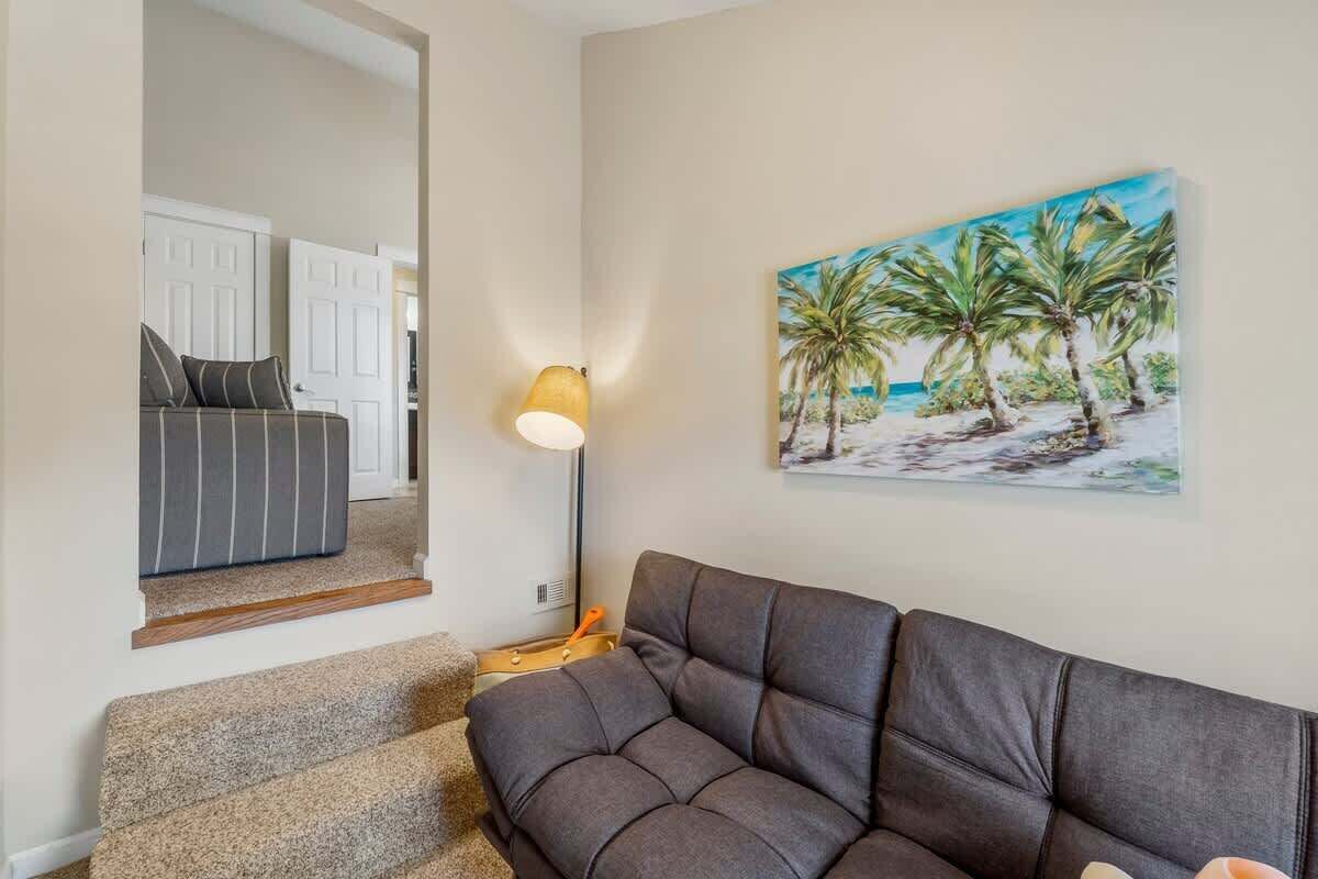 Un salon avec un canapé gris foncé, un tableau représentant une scène de plage et une lampe sur une table d’appoint.