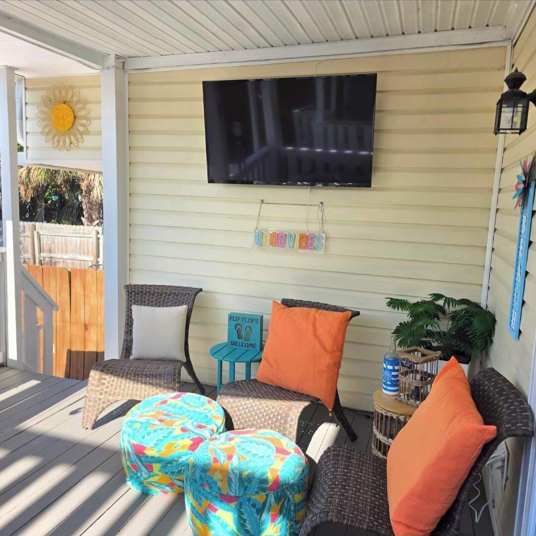 A covered porch with outdoor seating, a TV mounted on the wall, and a 'GOODVIBES' sign.