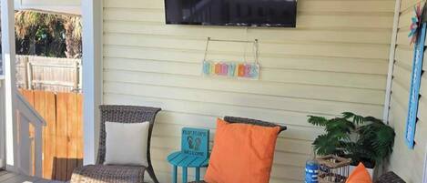 A covered porch with outdoor seating, a TV mounted on the wall, and a 'GOODVIBES' sign.