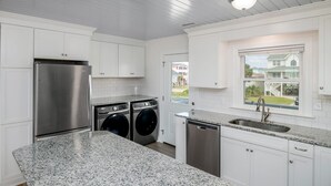 A modern kitchen with white cabinetry, stainless steel appliances, granite countertops, and a window with a view of a house. - 'Pop's Inn" - Oceanfront Home, 4 Bedrooms / 2 Bathrooms (Holden Beach)