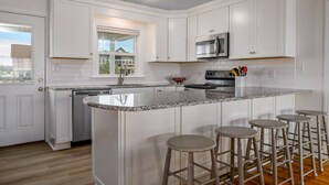 A kitchen with white cabinets, a granite countertop, a built-in microwave, and a large island with bar stools. - 'Pop's Inn" - Oceanfront Home, 4 Bedrooms / 2 Bathrooms (Holden Beach)