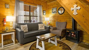 A cozy log cabin interior with a sofa, armchair, and a wood-burning stove. - Secluded Smokies Cabin | Private Pond + Hot Tub + King Bed (Sevierville)