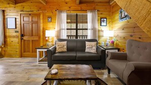 A cozy log cabin interior with a wooden floor, a sofa, a loveseat, and a coffee table. - Secluded Smokies Cabin | Private Pond + Hot Tub + King Bed (Sevierville)