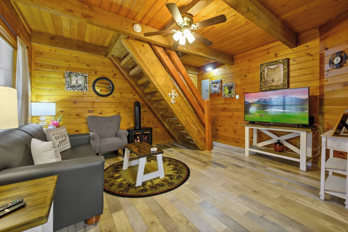 A cozy log cabin interior with a fireplace, a television, a sofa, and a staircase.