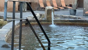 A building with a water feature in front, including a metal staircase leading into the water, and outdoor seating with chairs and tables.