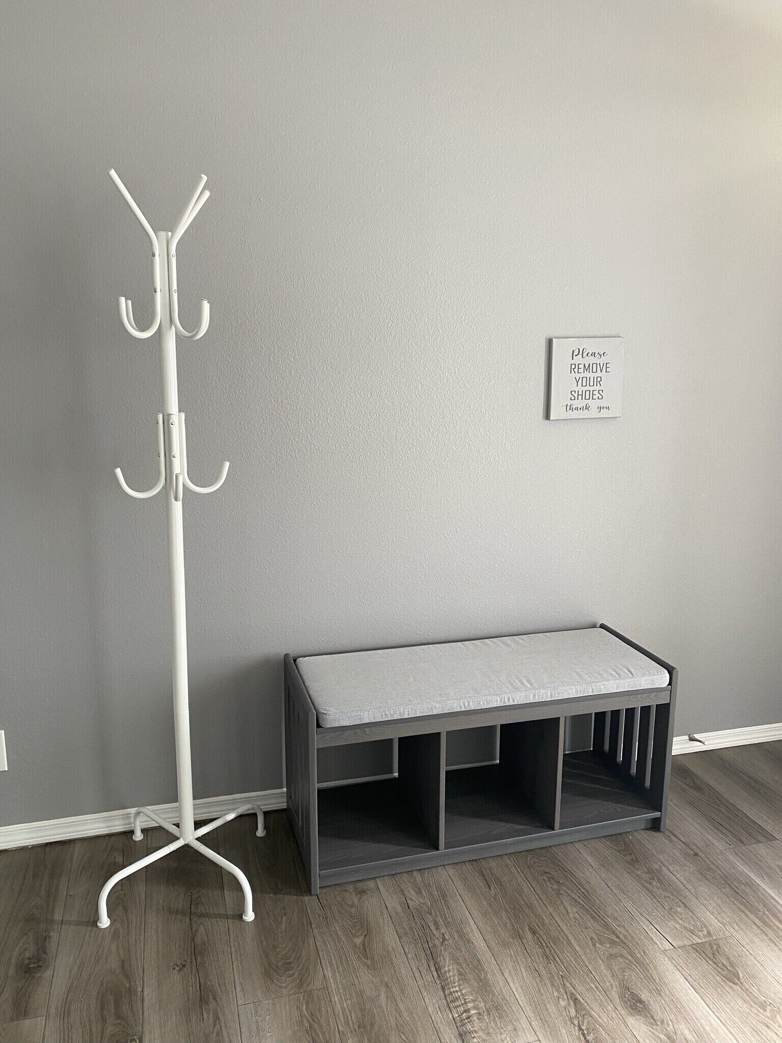 A room with a white coat rack, a grey bench, and a sign on the wall.
