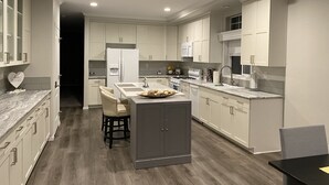A modern kitchen with white cabinetry, a central island, and a dining area with chairs.