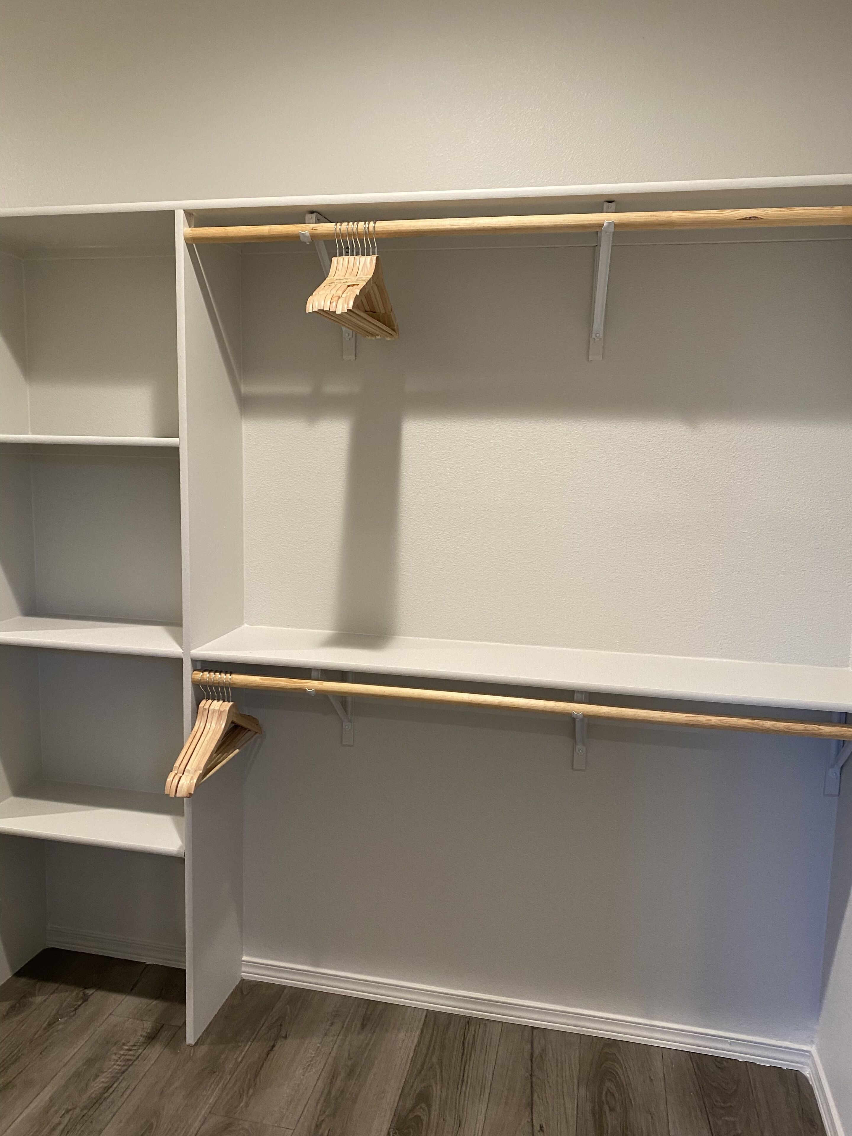 A corner of a room with a built-in closet featuring open shelves and a wooden rod for hanging clothes.