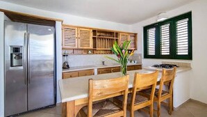 A kitchen with a central island, wooden chairs, a refrigerator, and a window with shutters.
