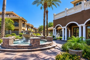 A courtyard with a central fountain, palm trees, and a building with a balcony. - 11 Bedroom / 8 Bath at TPC Scottsdale (Scottsdale)