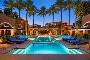 A pool area with lounge chairs and umbrellas, surrounded by palm trees and buildings.