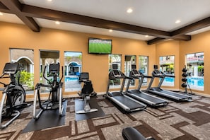 A fitness center with treadmills, elliptical machines, and a TV screen displaying a sports event.