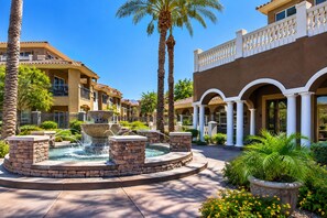A courtyard with a central fountain, palm trees, and a building with a balcony. - 1 Bedroom / 1 Bath Condo at TPC Scottsdale (Scottsdale)