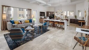 Amplia sala de estar con sofá, mesa de centro y sillas. Zona de cocina con mesa y sillas de comedor.