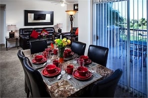 A dining area with a table set for four, surrounded by black leather chairs, a vase with flowers, and a modern lamp.