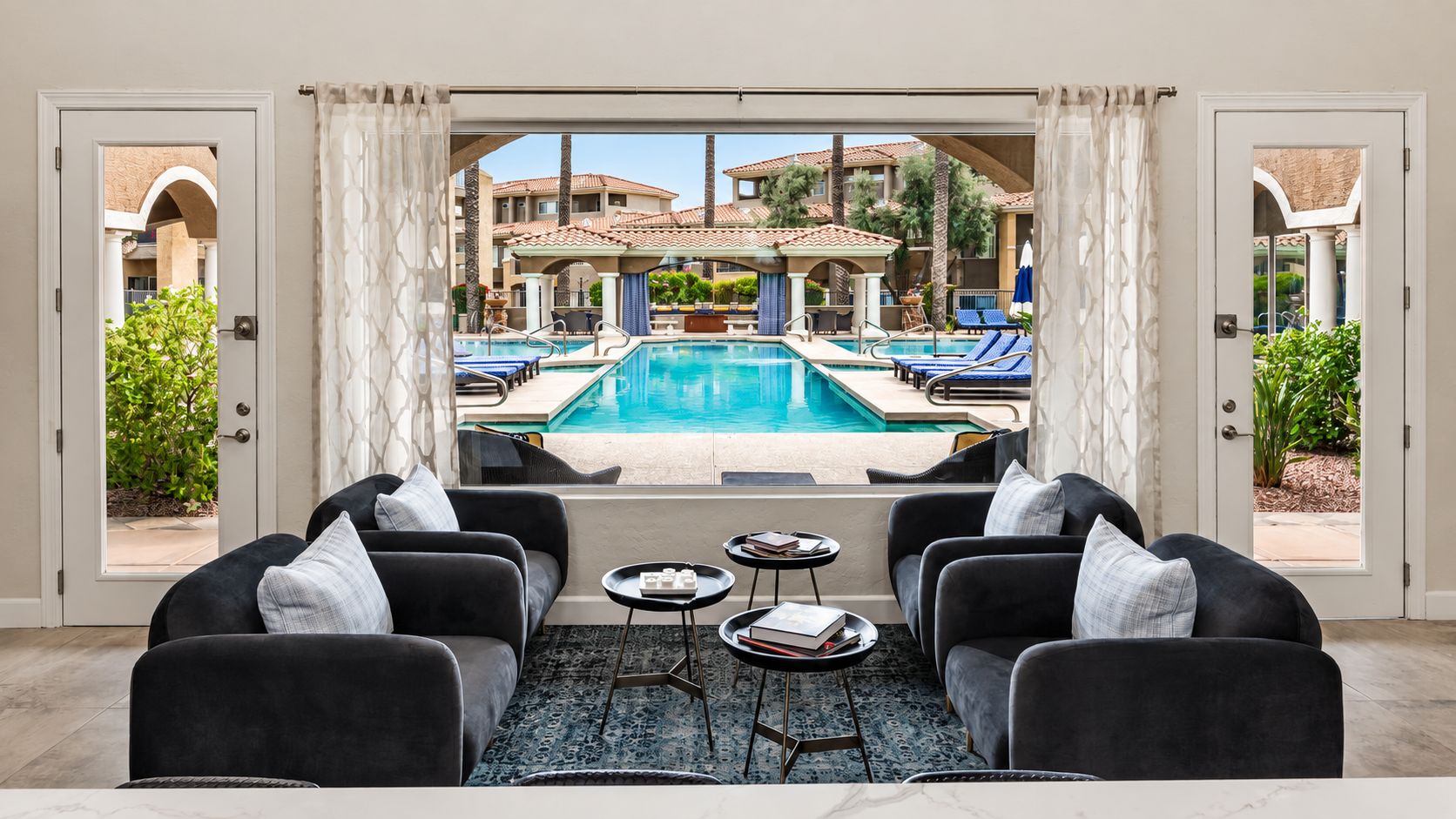 A poolside seating area with a view of a swimming pool, outdoor furniture, and a patio with umbrellas.