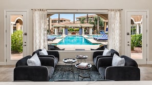 A poolside seating area with a view of a swimming pool, outdoor furniture, and a patio with umbrellas.