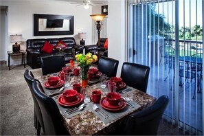 A dining area with a table set for four, surrounded by black leather chairs, a vase with flowers, and a modern lamp.