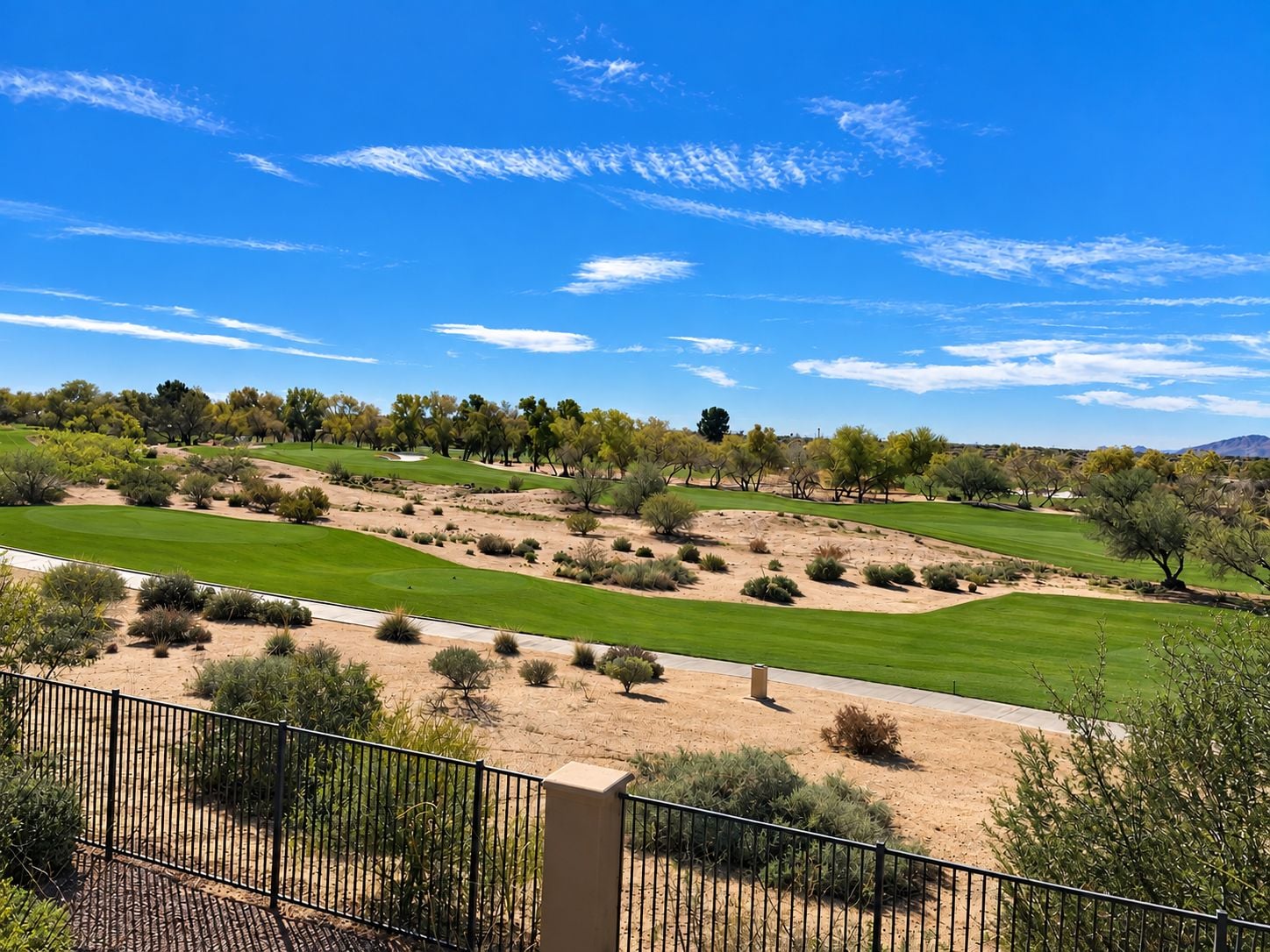 A golf course with sand bunkers, a clear sky, and a fence in the foreground.