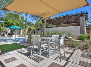 Une terrasse extérieure avec des tables et des chaises en métal, une piscine et une pergola surmontée d’une toiture.