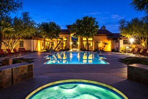 Una piscina con sillas de descanso y un jacuzzi, rodeada por un jardín ajardinado y un edificio con tejado de azulejos.