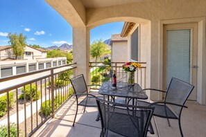 A balcony with a table and chairs, a vase with flowers, and a bottle of wine.