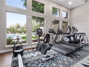 A home gym with treadmills and a stationary bike, large windows, and a view of a swimming pool.